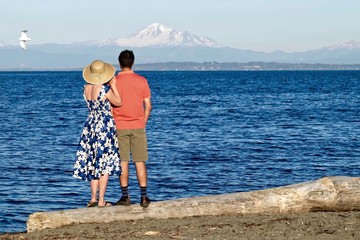 Married couple on beach huggin and looking at view of snow capped volcano. Centennial Beach in...