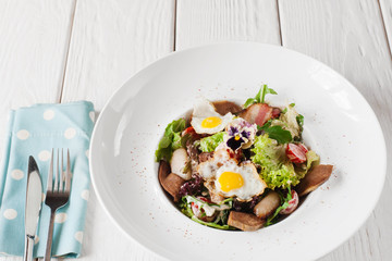Salad with tongue and quail eggs on white wooden background. Restaurant serving of meat side dish with cutlery, armenian cuisine