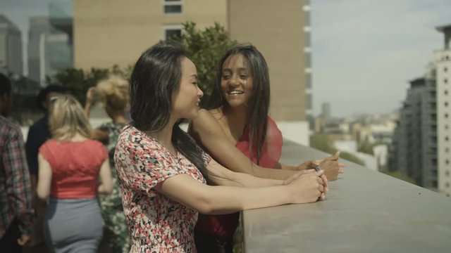  Happy female friends chatting & looking at view at rooftop party