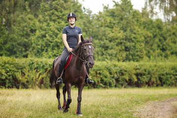 Girl riding a horse. Girl in dark helmet, jeans and high boots on a brown horse