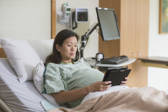 Pregnant Chinese Woman In Hospital Room Using Digital Tablet