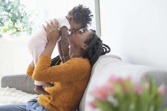 Black woman kissing nose of baby daughter on sofa