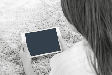 Closeup tablet computer on asian woman hand on blurred gray carpet floor textured background with copy space in black and white tone