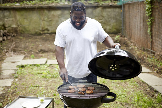 Black man grilling hamburgers at backyard barbecue