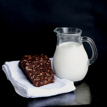 Jug of milk, sliced rye bread and cotton napkin on black bacgoung, special light.