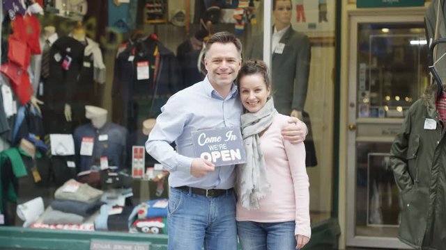  Happy business partners outside shop hold up a sign to show they are open