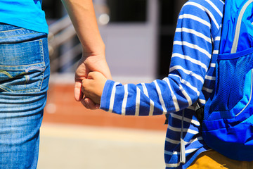 Mother holding hand of little son with backpack, back to school