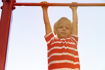 little boy playing on monkey bars in playground