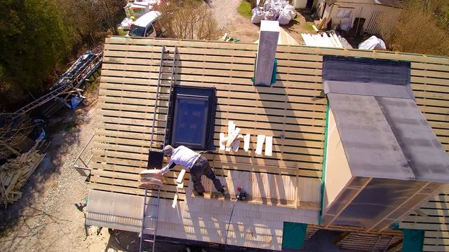 A roofer putting on the wooden shingles on the roof it is a newly constructed wooden house.