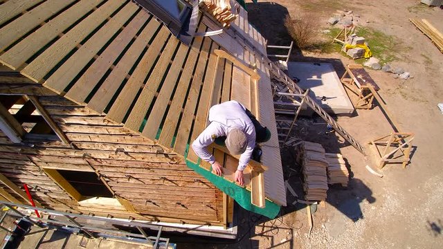 Closer look of the roofer installing the shingles on the wooden roof of the cabin house