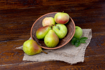 still life of fruit: apples and pear on a plate with mint leaves with wooden background
