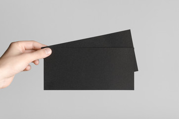 Black DL Flyer Mock-Up - Male hands holding black flyers on a gray background.