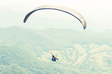 One paraglider on summer day over the green hills