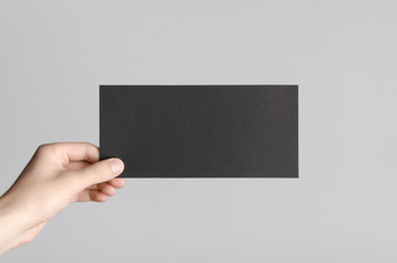 Black DL Flyer Mock-Up - Male hands holding a black flyer on a gray background.