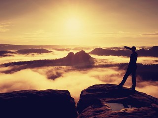 Naklejka na ściany i meble Tall hiker in black enjoing orange sunrise on view point. Heavy mist bellow in valley.