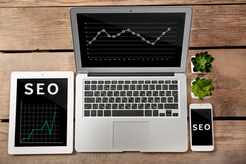 SEO technology concept. Laptop, tablet and phone on wooden background.