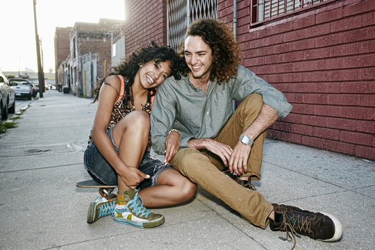 Couple sitting on skateboard on city street