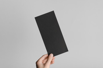 Black DL Flyer Mock-Up - Male hands holding a black flyer on a gray background.