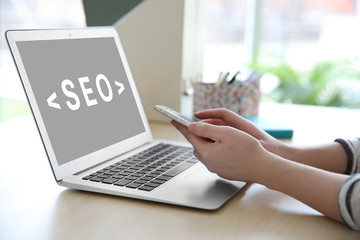 SEO technology concept. Woman using phone and laptop in office.
