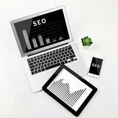 SEO technology concept. Laptop, tablet and phone on white wooden background.