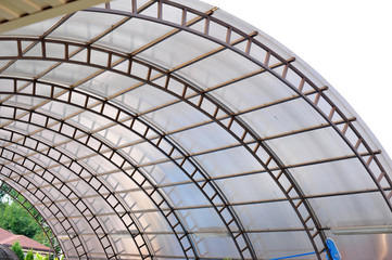 A canopy made of polycarbonate arc against the blue sky. Metal construction.
