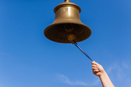 A small bell in the girl's hand on a neutral background, close-up, Concept:  the first bell, a ringing bell. Stock Photo