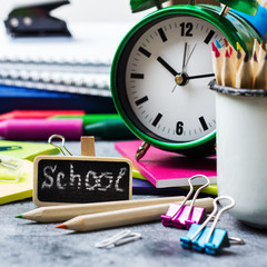 School stationery, pencil, pen, note, alarm clock on grunge chalkboard