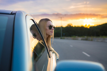 The girl in the car against the background of a road and picturesque sunset