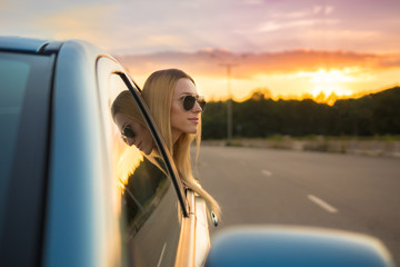 The girl in the car against the background of a road and picturesque sunset