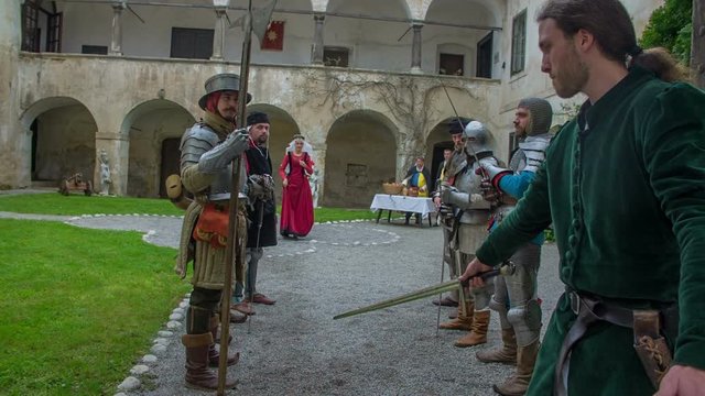 The knights and the members of the royal family are bowing when an important guest enters into a castle. Close-up shot.
