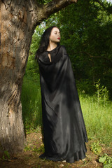 Beautiful brunette woman in black dress and black cloak in the m