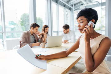 Fototapeta premium Serious businesswoman with documents talking on cell phone in office