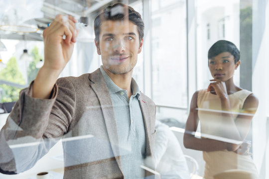 Businessman working with businesswoman and writing on transparent board