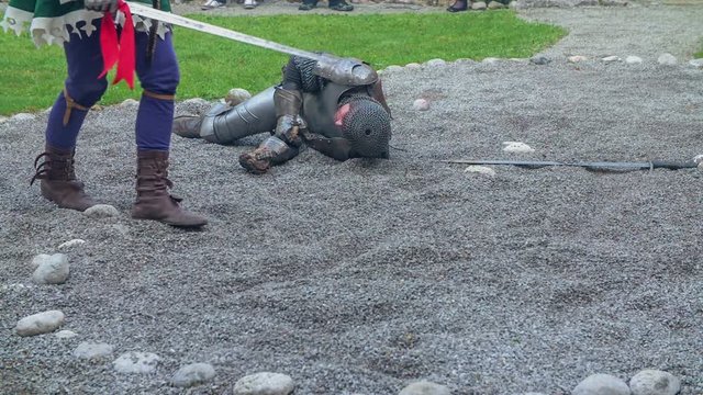 Knights are passing a motionless knight that is lying on the ground in the courtyard. Close-up shot.
