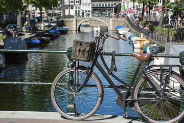 Fototapeta na wymiar One bike with basket on the pavement near the bridge over the canal in the sunlight in Amsterdam