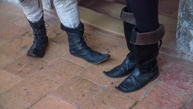 Two people are talking and bothe of them are wearing black medieval boots. Close-up shot.

