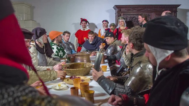 A princess is making a toast for the knights before they start eating dinner. Everyone lifts their glasses up in the air. Close-up shot.
