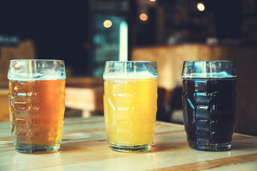 Beautiful background of the Oktoberfest. Glasses of cold fresh white, light and dark beer on the wooden bar counter in the pub. Assorted alcohol in a Flight Ready for Tasting