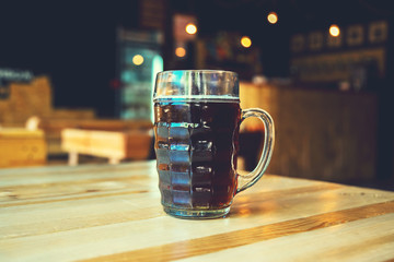 A chilled glass of fresh dark beer on the wooden bar counter in pub with free space for your text. Beautiful background of the Oktoberfest.