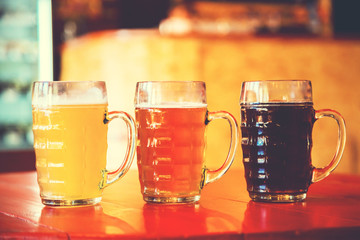 Beautiful background of the Oktoberfest. Glasses of cold fresh white, light and dark beer on the wooden bar counter in the pub. Assorted alcohol in a Flight Ready for Tasting