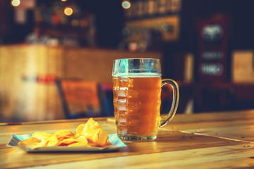 A fresh glass of cold light beer and potato chips on the wooden bar counter in pub with free space...