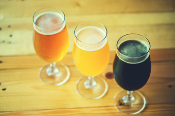 Beautiful background of the Oktoberfest. Glasses of cold fresh white, light and dark beer on the wooden bar counter in the pub. Assorted alcohol in a Flight Ready for Tasting