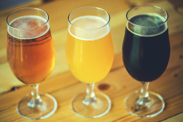 Beautiful background of the Oktoberfest. Glasses of cold fresh white, light and dark beer on the wooden bar counter in the pub. Assorted alcohol in a Flight Ready for Tasting