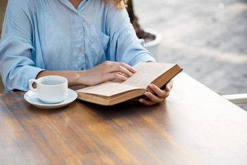 Obraz premium Hands of young girl sitting at the table with book and coffee cup. 