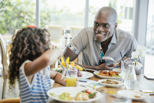 Smiling Father And Daughter Eating Food At Restaurant