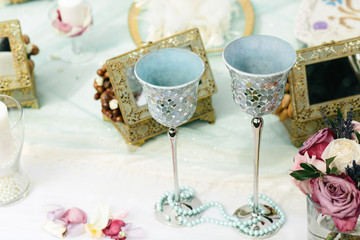 Delicate silver glasses stand behind a blue necklace on the tabl
