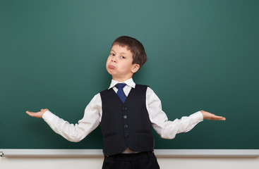 school student boy posing at the clean blackboard and open arms, grimacing and emotions, dressed in a black suit, education concept, studio photo