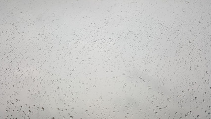 Closeup raindrops perched on the glass while it is raining.