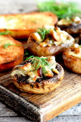 Stuffed mushrooms and fried toasts on a chopping board and wooden table. Baked mushroom caps stuffed with cheese and meat recipe. Closeup