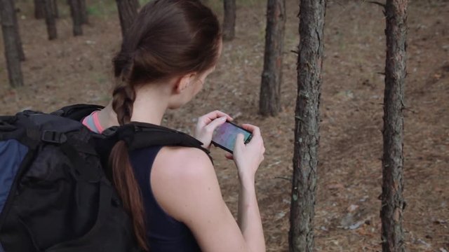 Woman tourist with backpack using navigation app on smartphone in the beautiful wild forest. Travel concept.